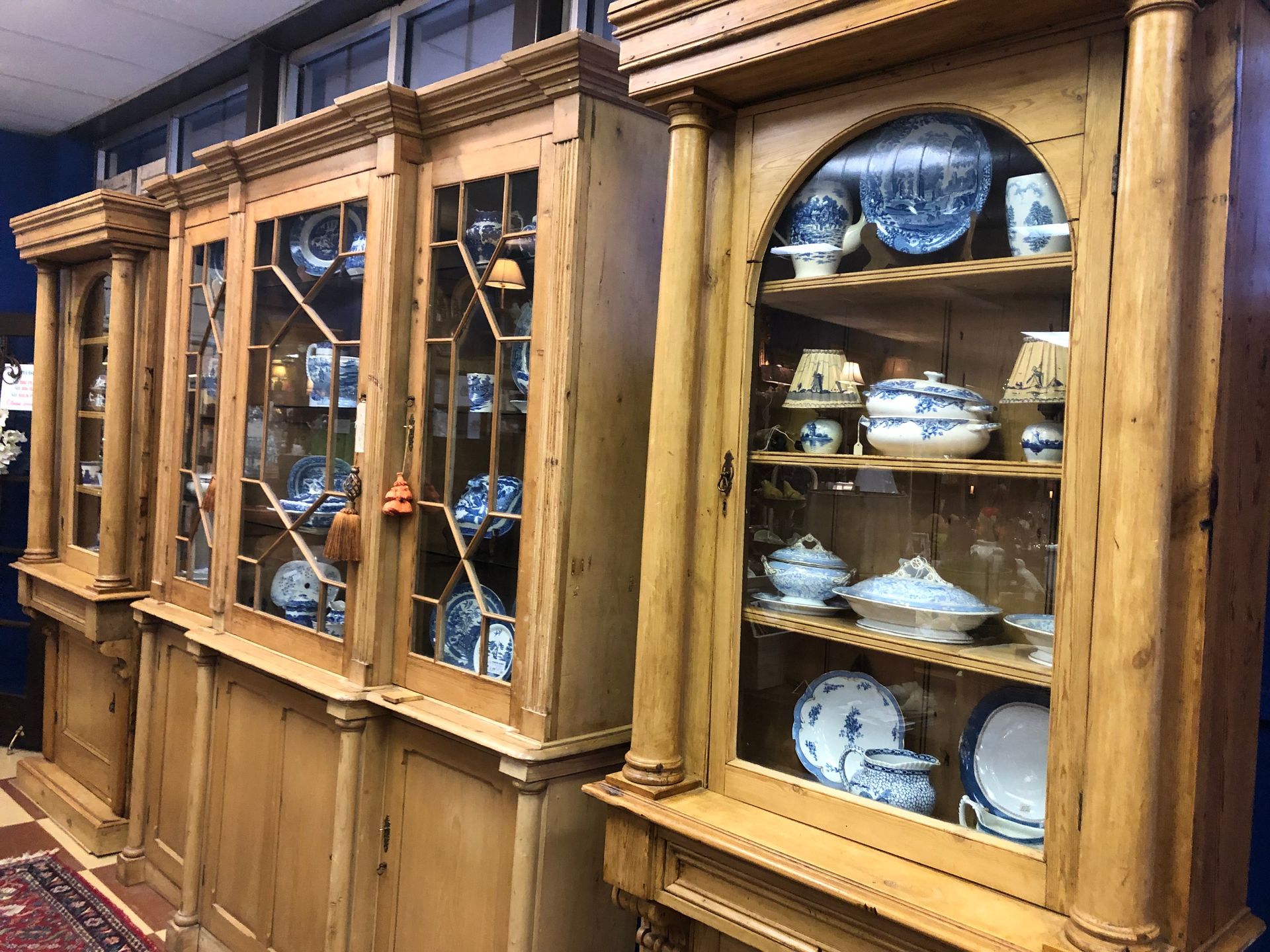 Wooden display cabinet with glass doors holding dishes and ceramics in a warmly lit room