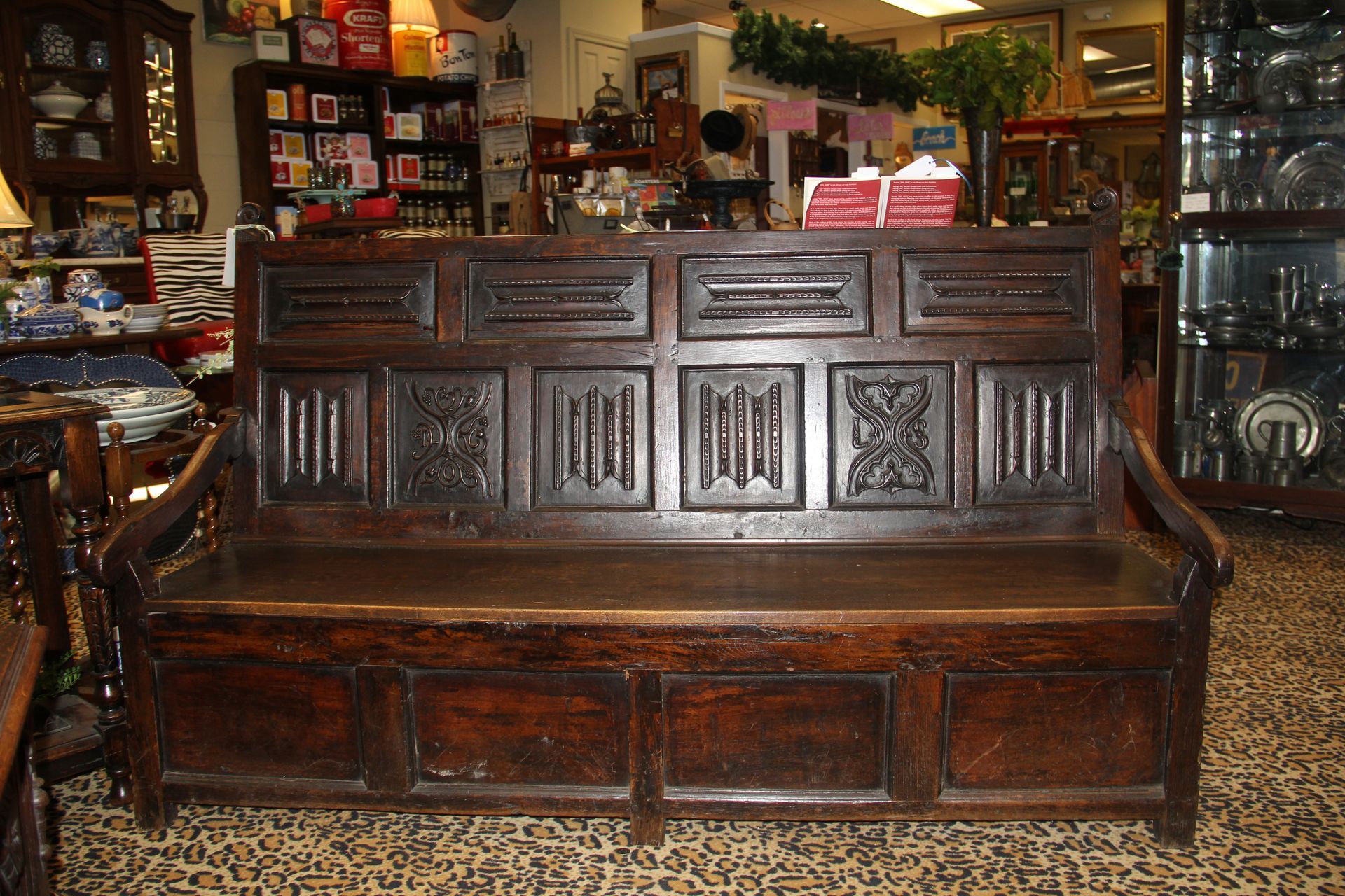 Dark wooden bench in a cluttered antique shop, with carved backrest and patterned tile floor
