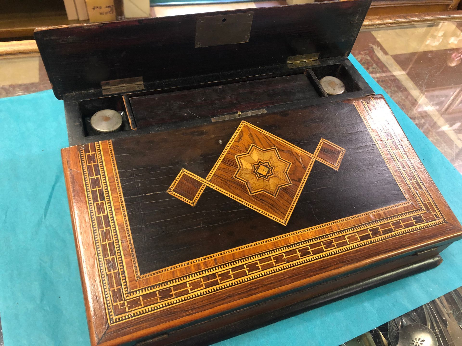 Ornate wooden writing desk with inlaid gold border and a hinged lid on a blue cloth background