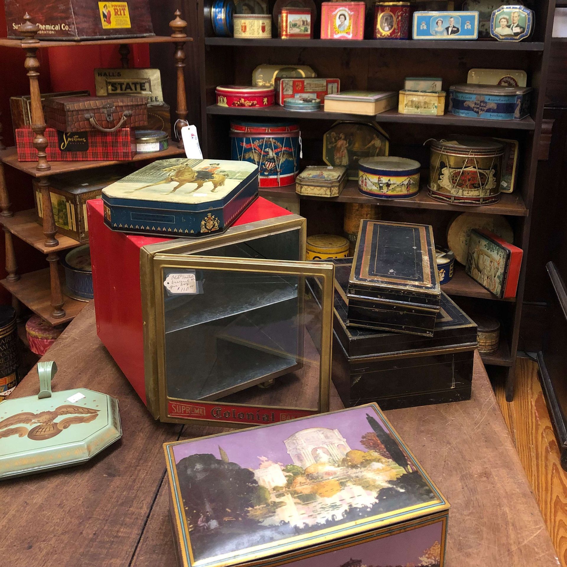 Vintage tins and decorative boxes arranged on wooden shelves and floor in a shop display.