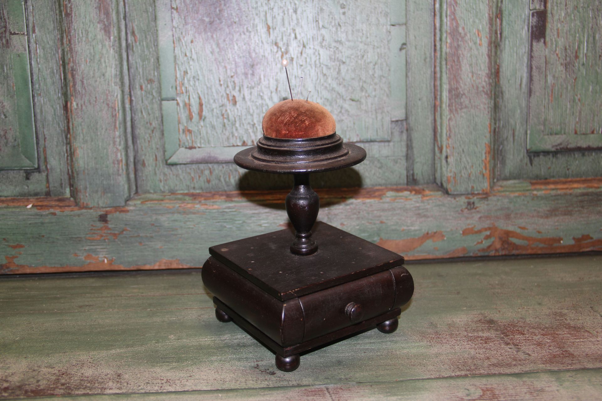 Small dark wooden stand holding a spherical, orange-brown object in front of a weathered green door.