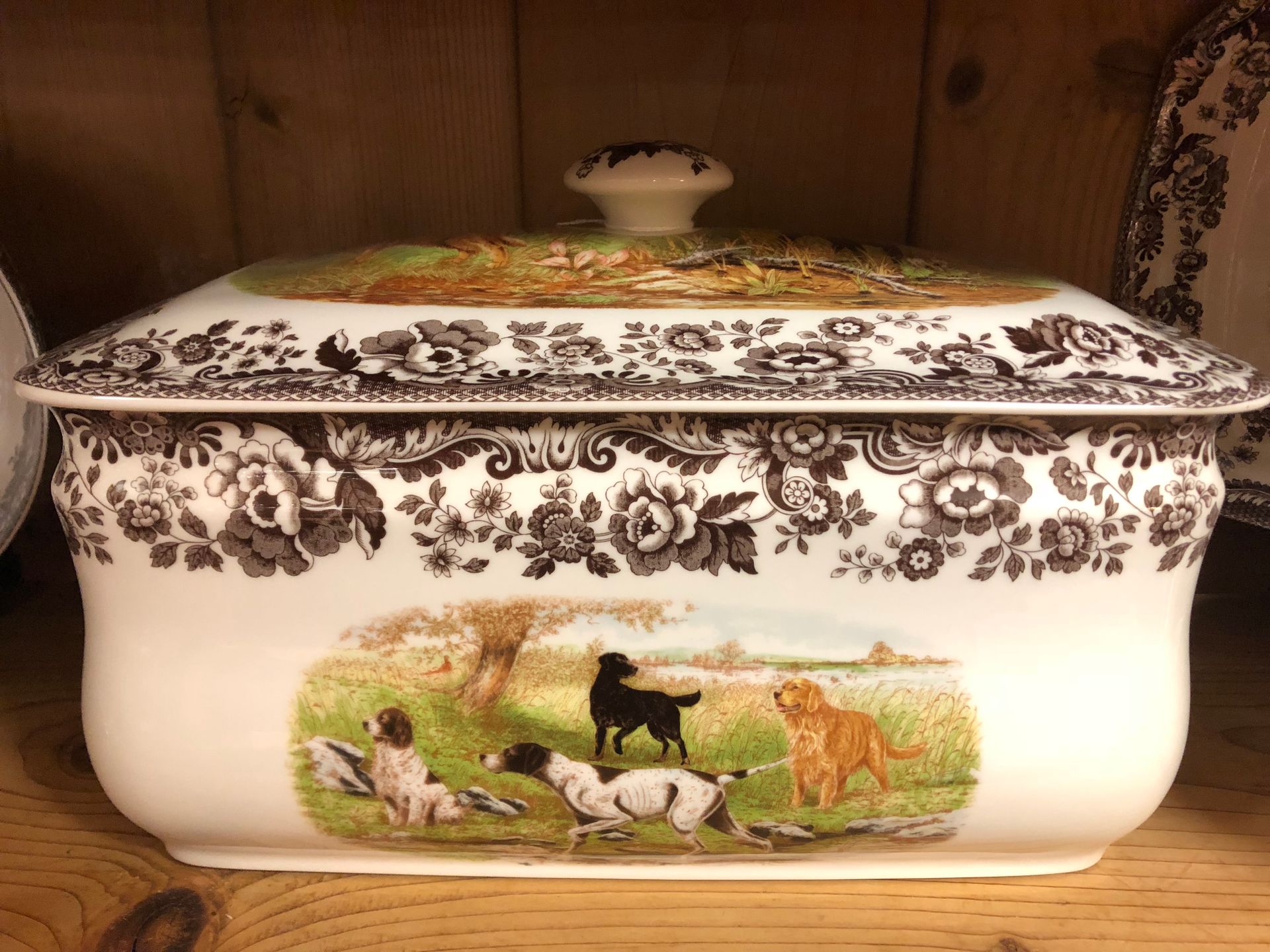 Decorative white porcelain casserole with brown floral border and painted pastoral animal scene on the front