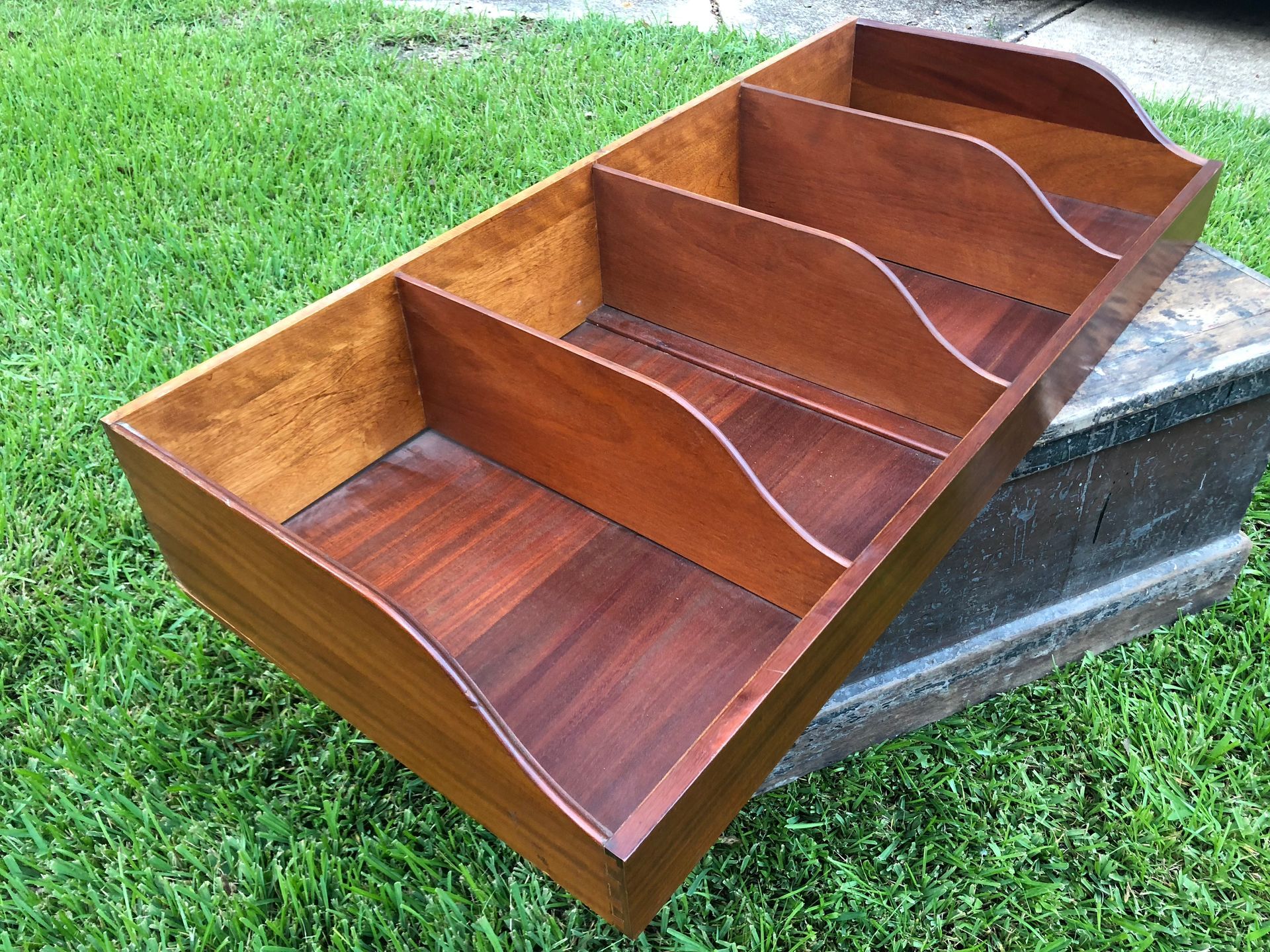 Wooden tabletop organizer with five slanted compartments on grass near a stone step