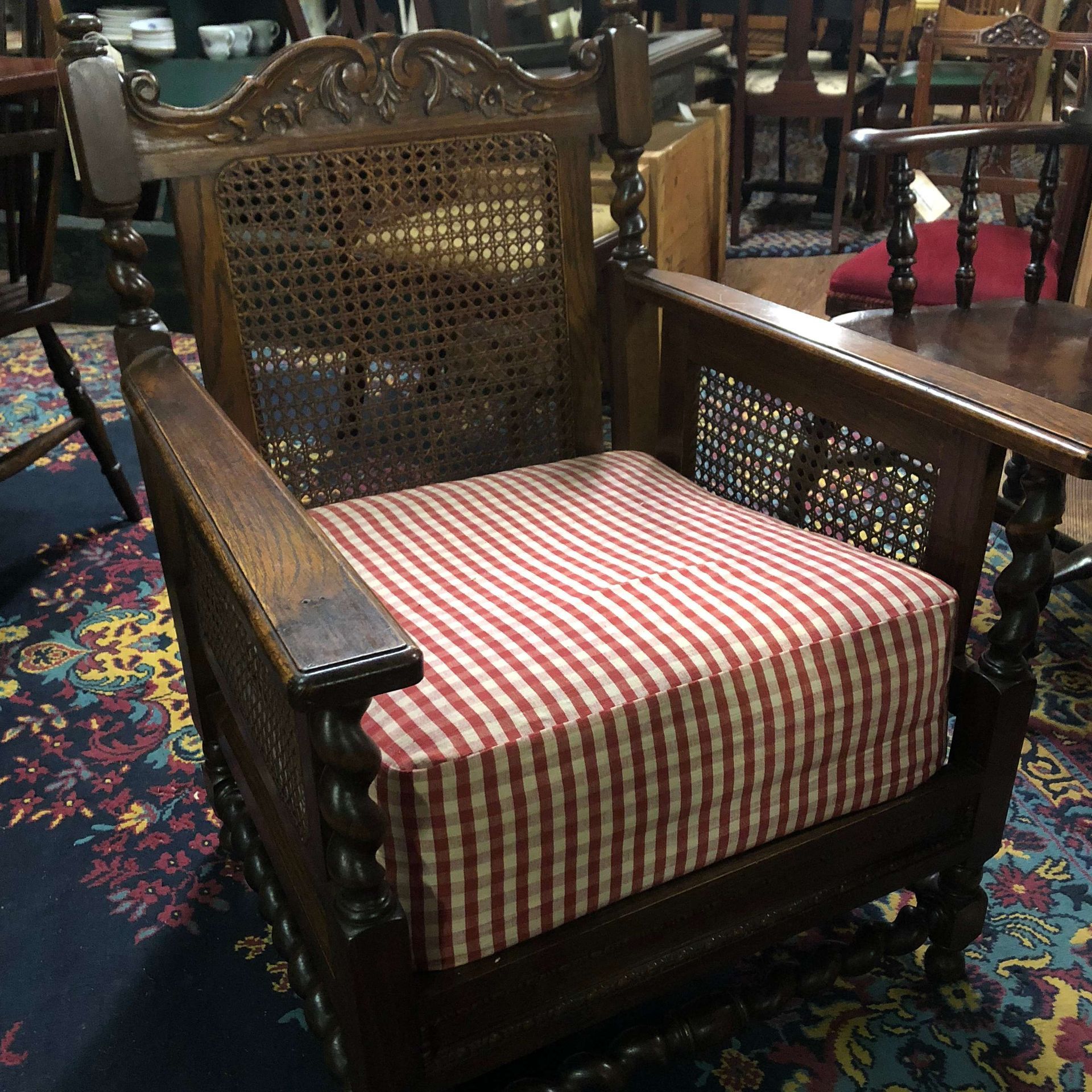 Wooden armchair with woven back and red-and-white striped cushion on a patterned carpet.