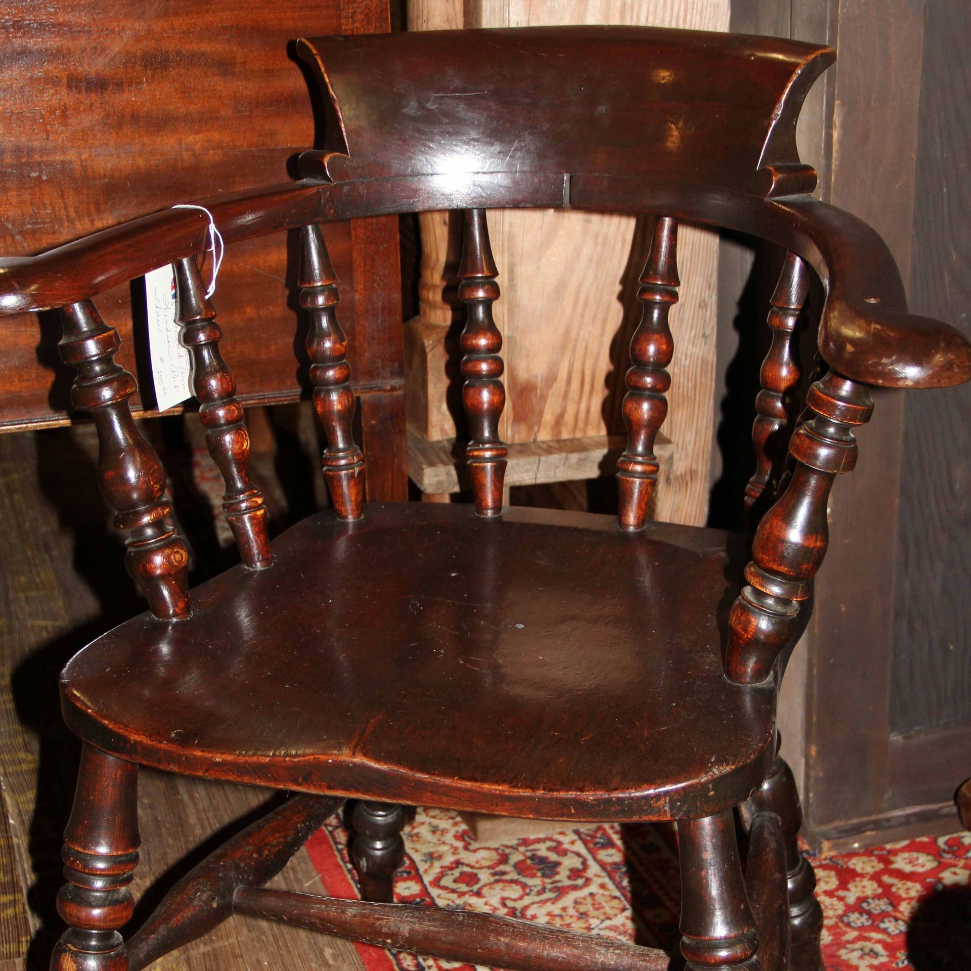 Dark wooden chair with turned spindles and curved back on a patterned rug against a wood wall.