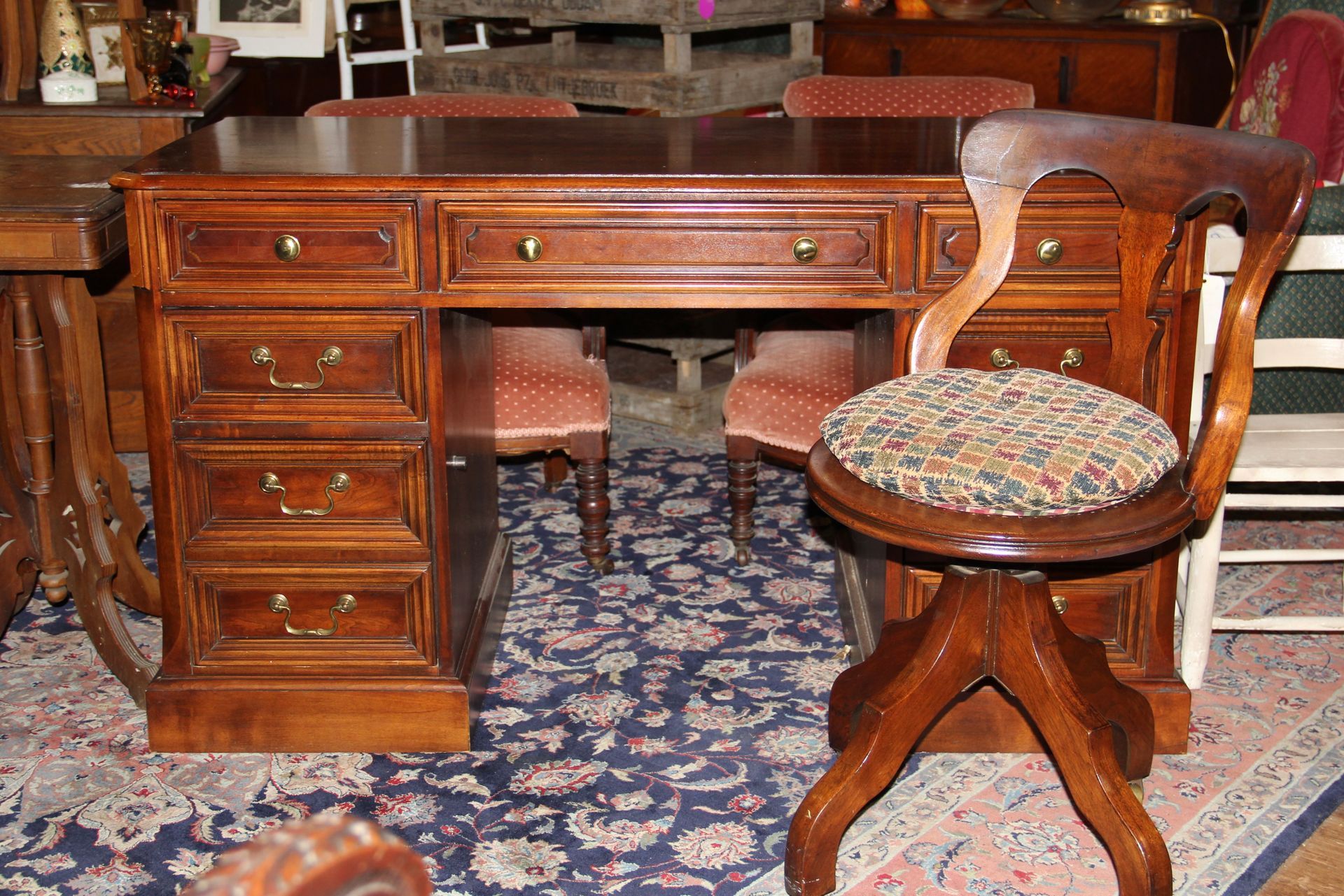 Antique wooden desk with drawers and patterned upholstered chair on a floral rug