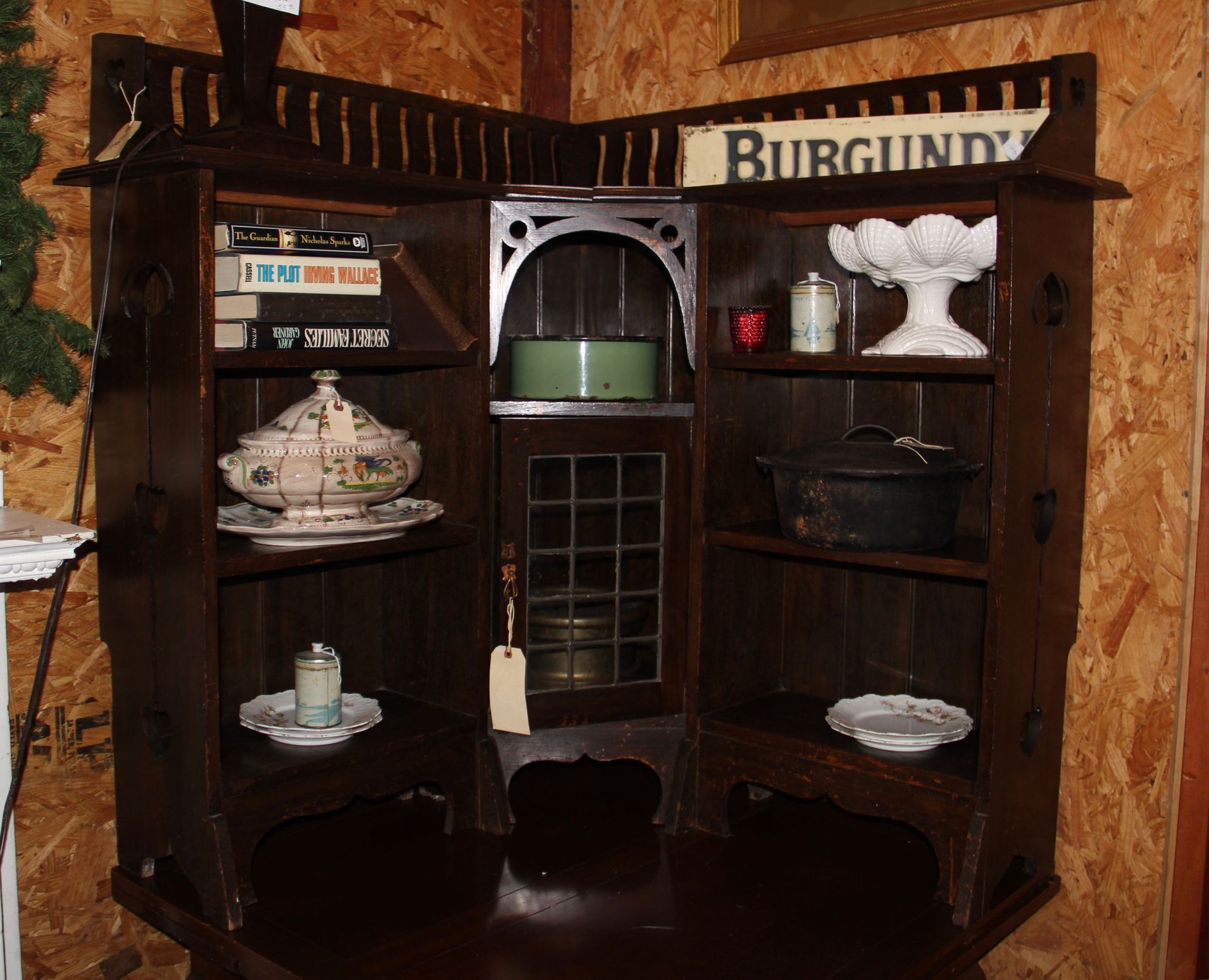 Rustic corner hutch with shelves of dishes and decor, labeled “Burgundy,” in a warm wood-paneled room