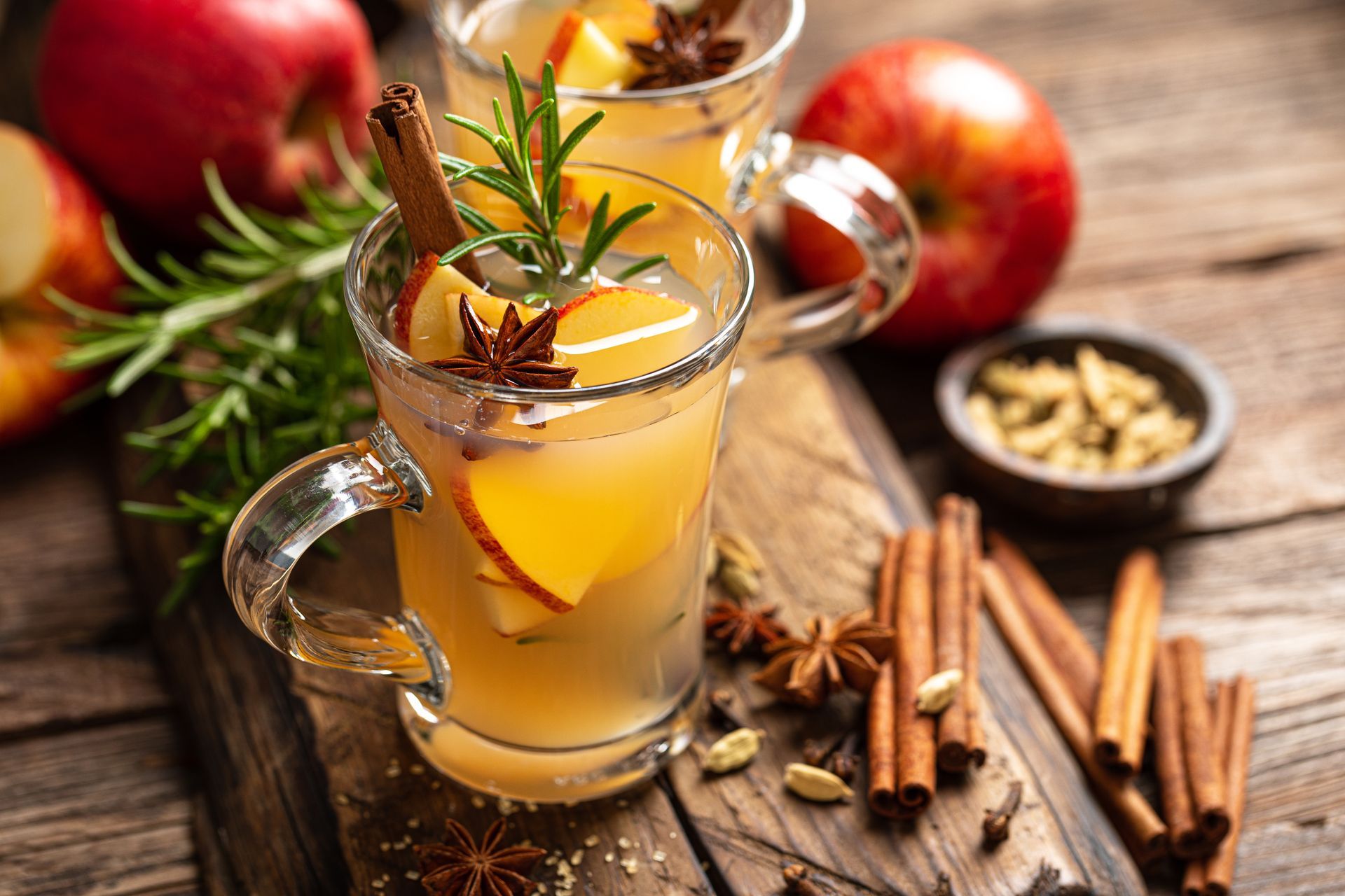 Two cups of apple cider with cinnamon sticks and star anise on a wooden table.