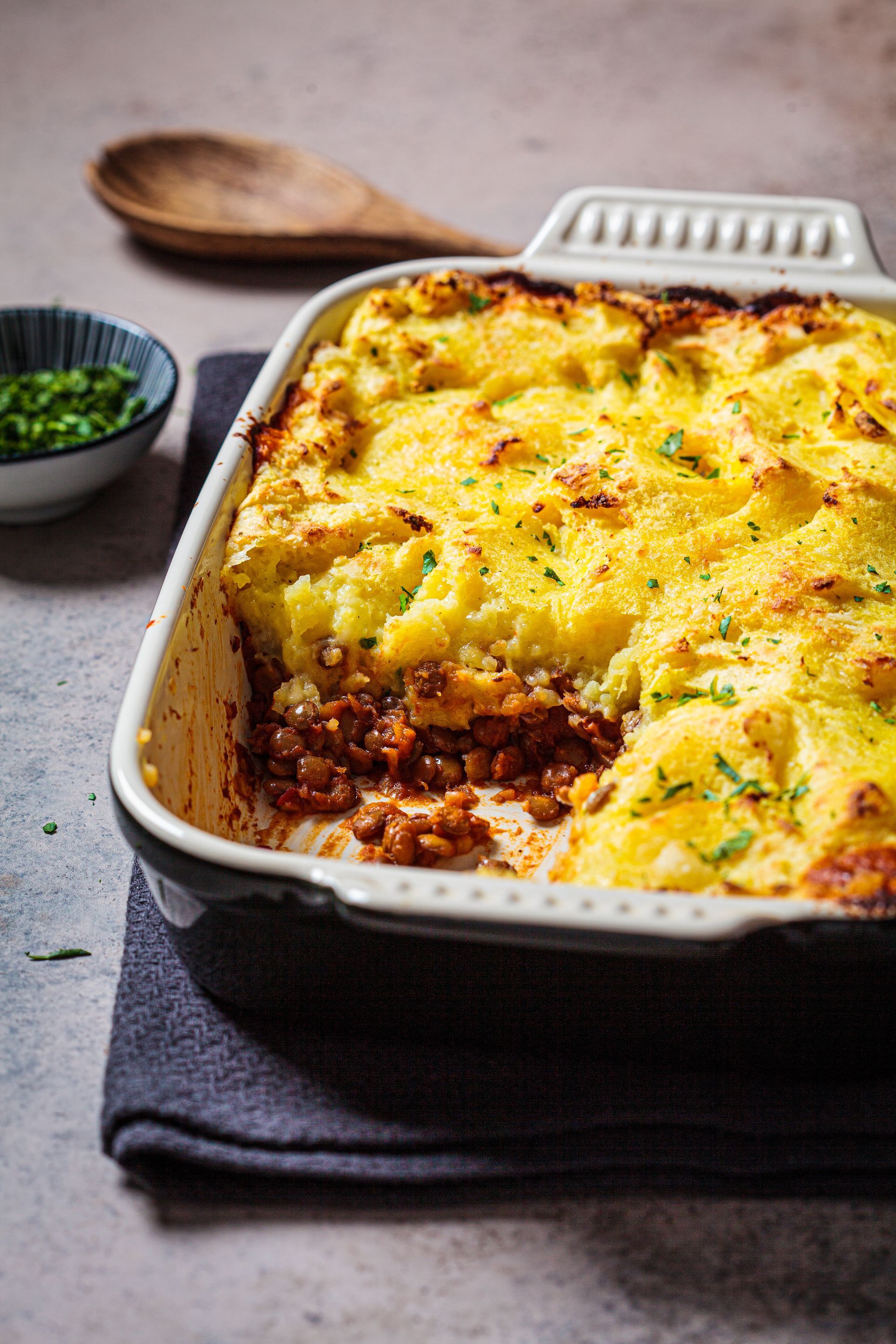 A casserole dish filled with shepherd 's pie with a spoon in the background.