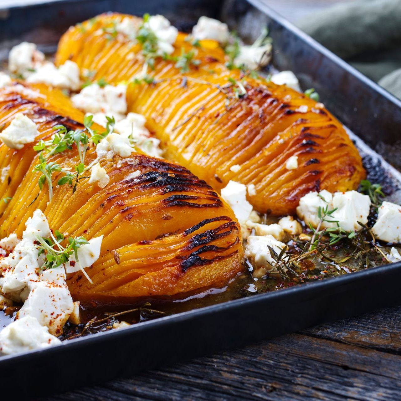 A tray of roasted butternut squash with feta cheese and thyme on a wooden table.
