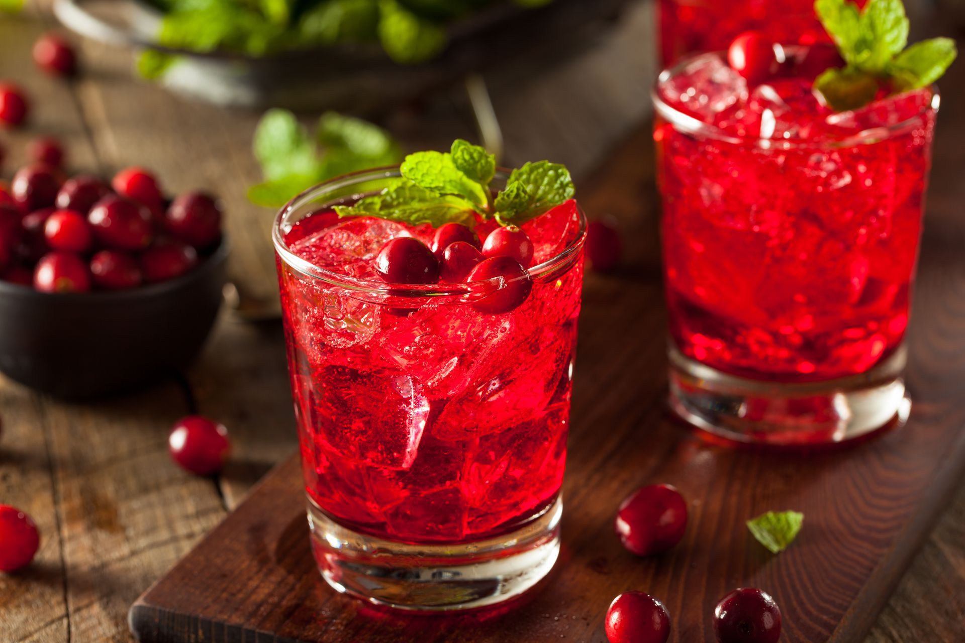 Two glasses of red liquid with cranberries and mint on a wooden table.