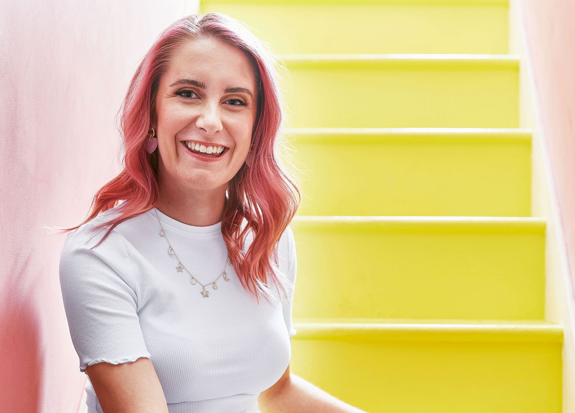A woman with red hair is smiling while sitting on a set of yellow stairs.