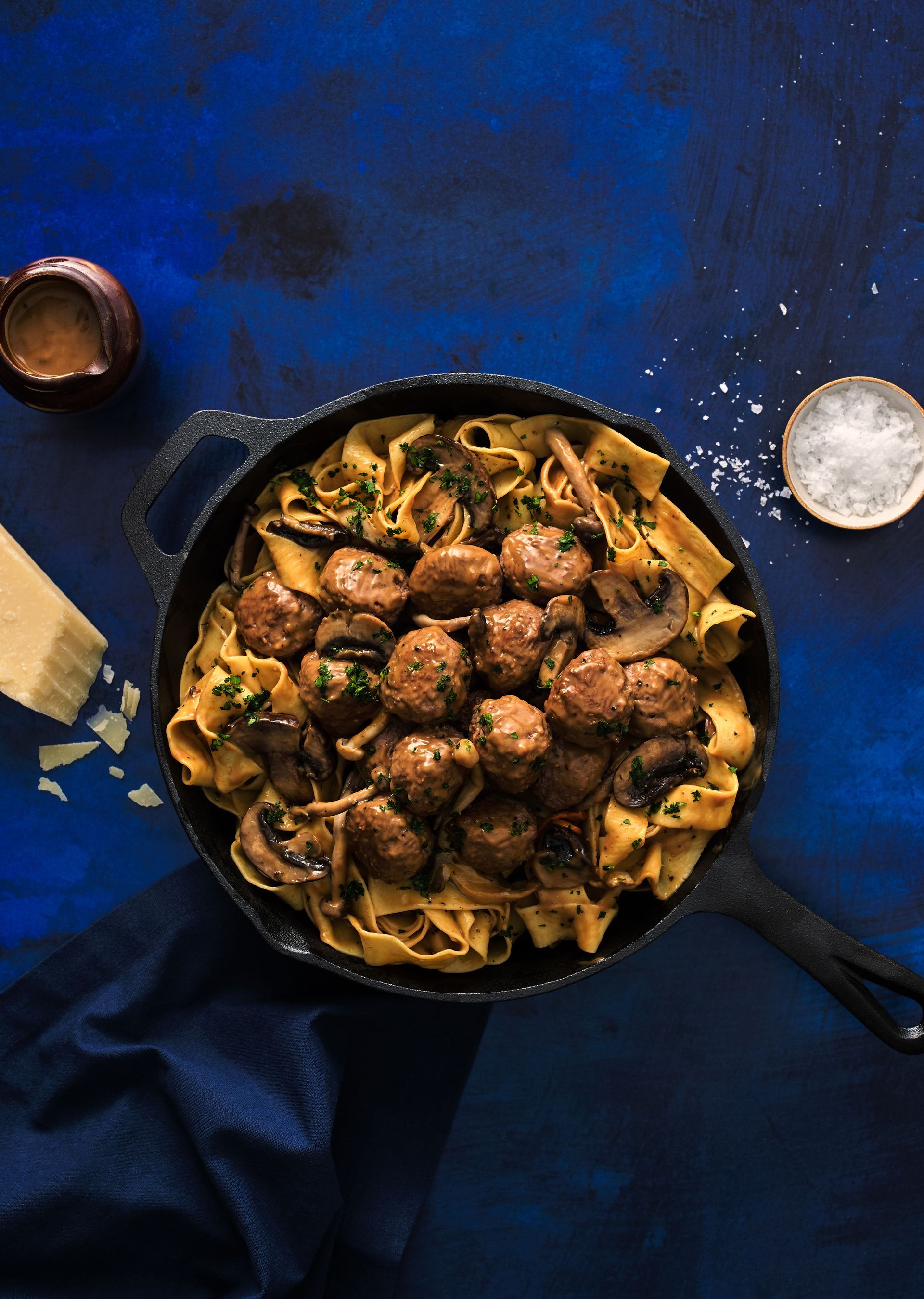 A pan filled with meatballs and noodles on a blue table.