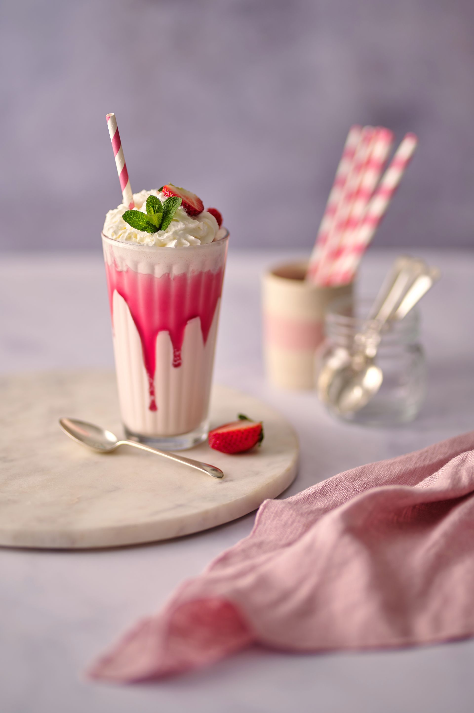 A strawberry milkshake with whipped cream and strawberries on a table.