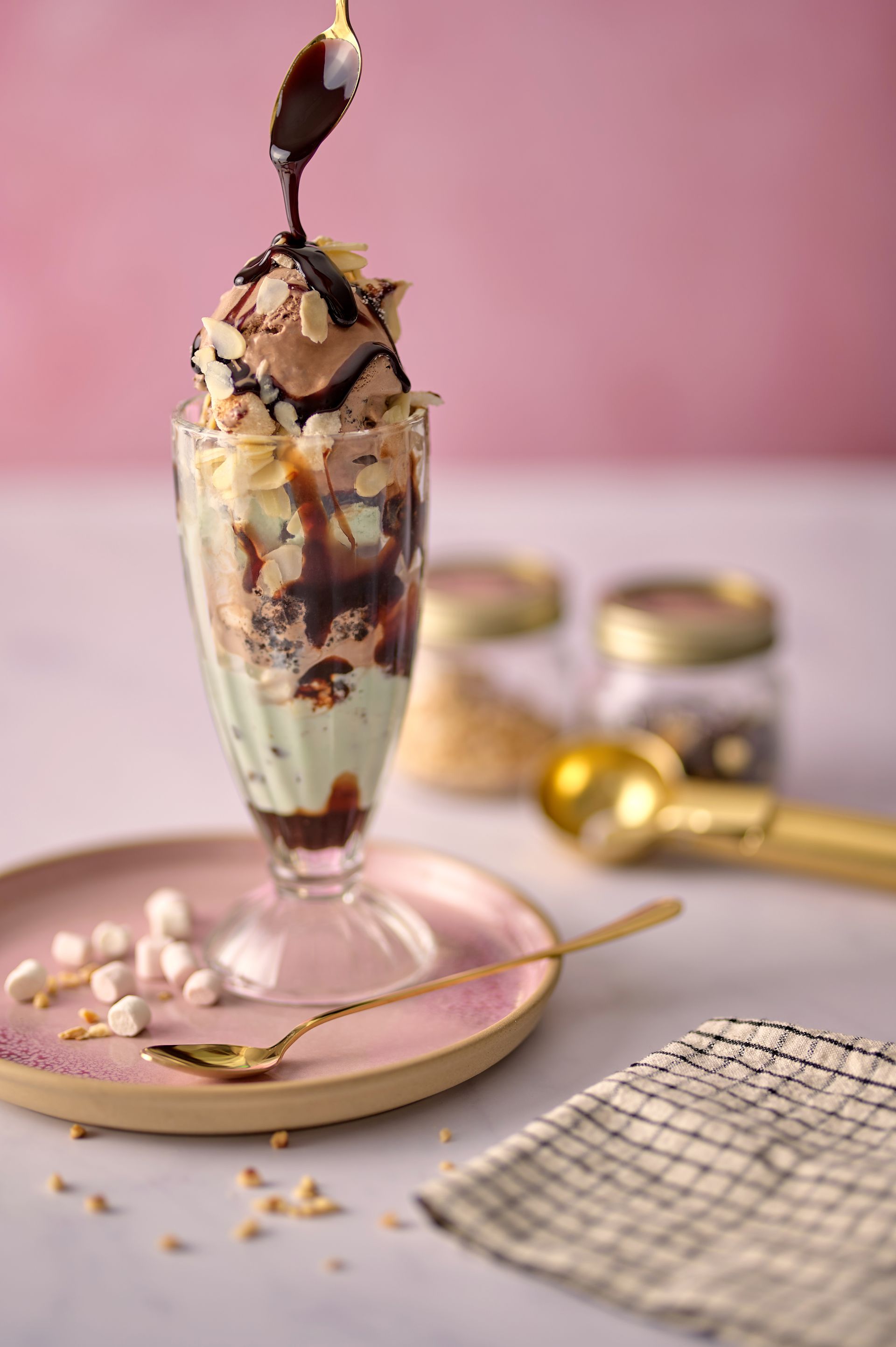 A close up of a sundae in a glass on a plate with a spoon.