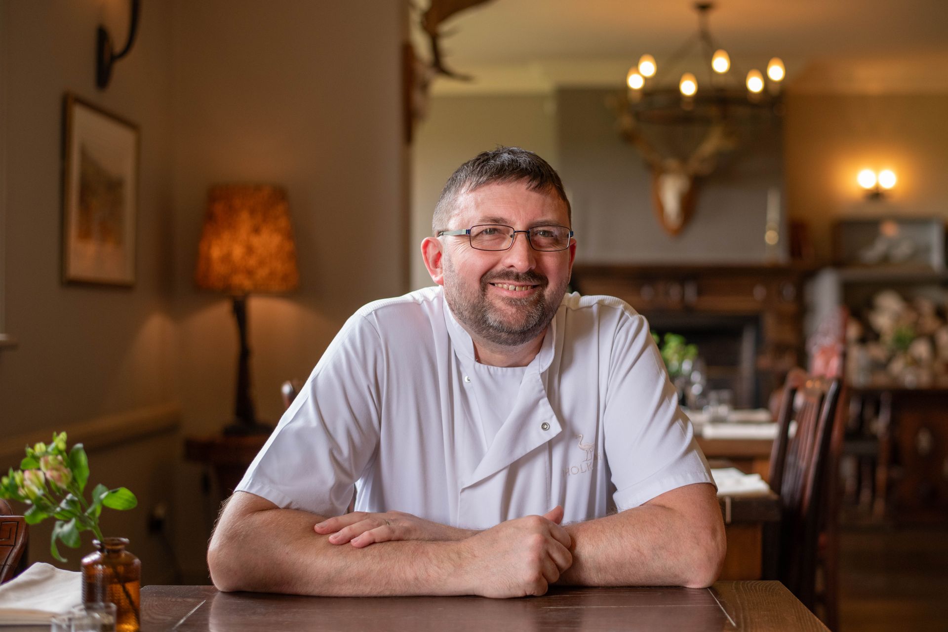 A man is sitting at a table in a restaurant with his arms crossed.