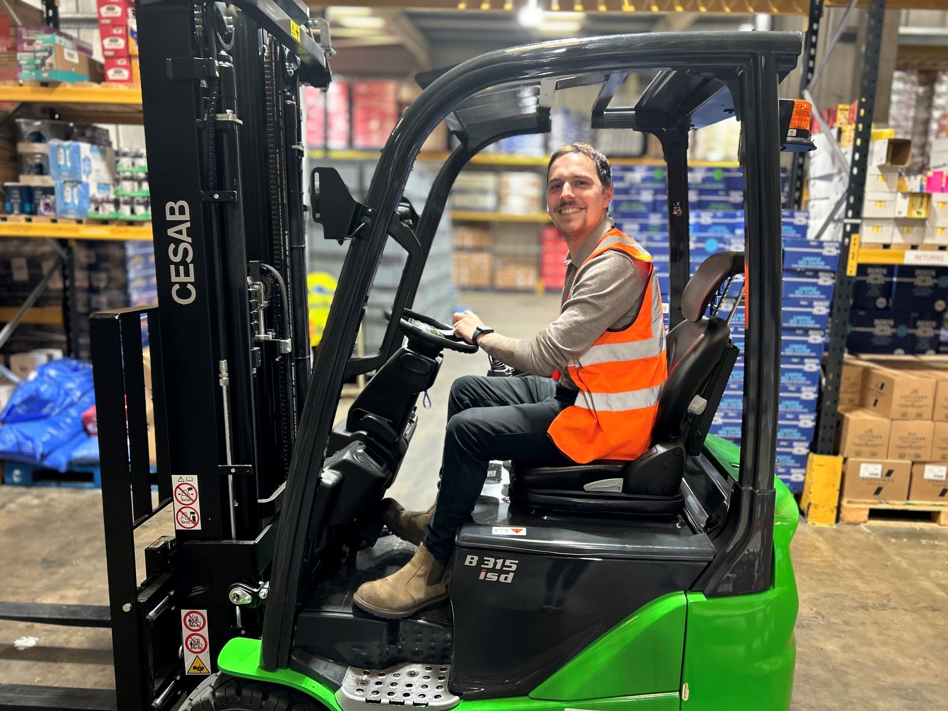 A man is sitting in a green forklift in a warehouse.