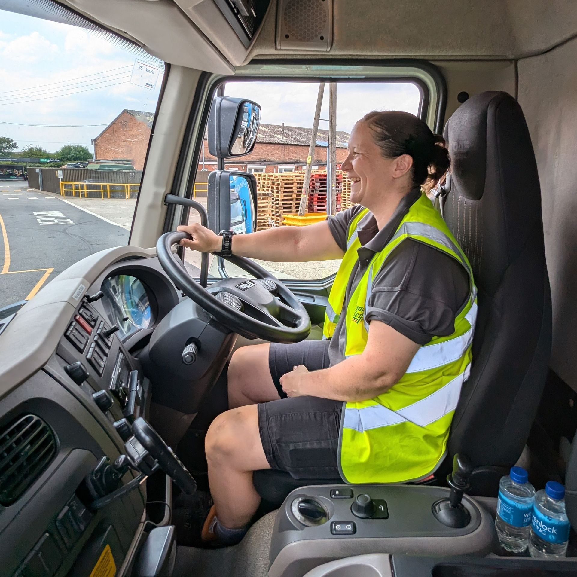 A woman in a yellow vest is driving a truck.