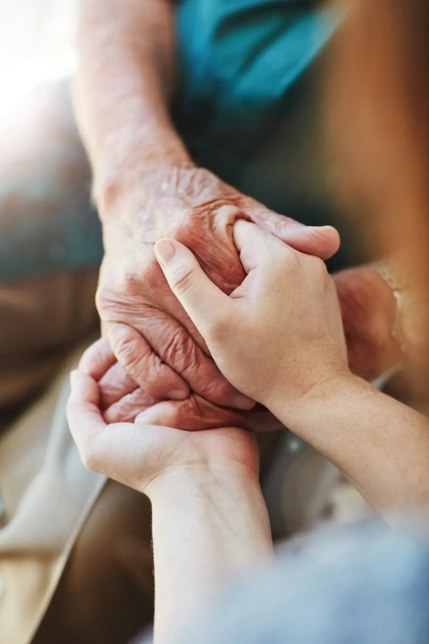 Hands gently holding each other in a close-up, with a soft, warm background.