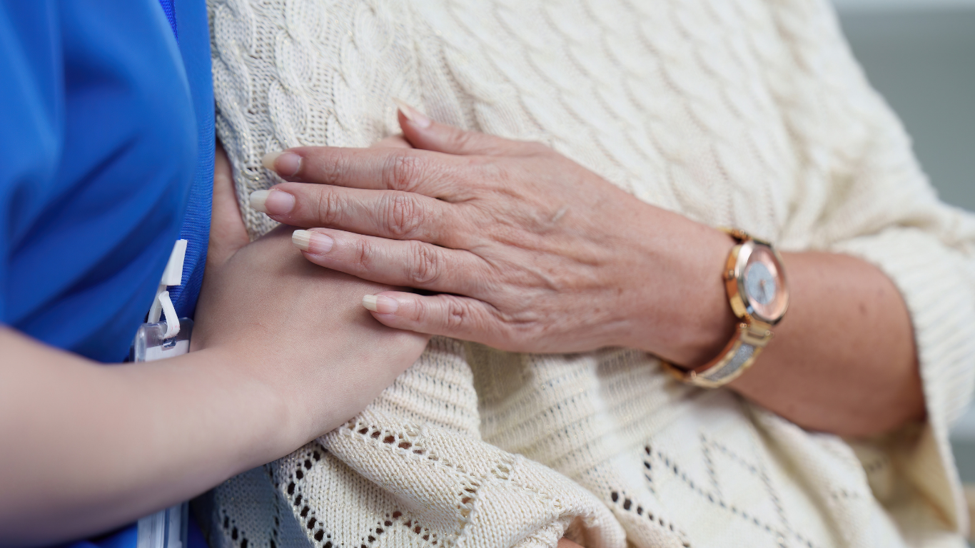 Hands gently clasping an older person’s arm over a cream knit blanket
