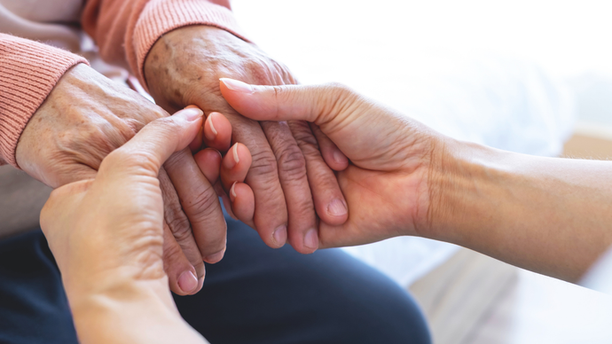 Two people gently holding an older person’s hands in a supportive gesture