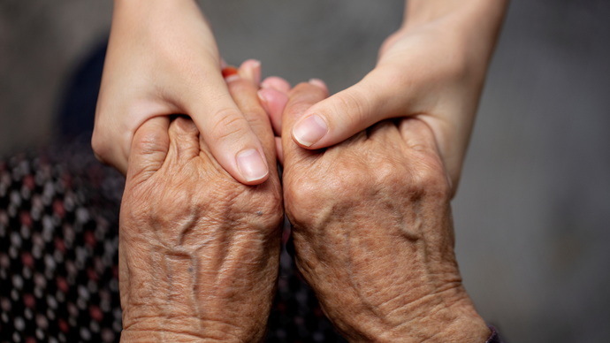 Two hands gently holding an elderly person’s wrinkled hands in a close-up.