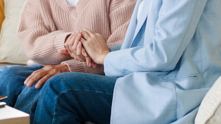 Two people sit close together, holding hands, in soft pink and blue sweaters.