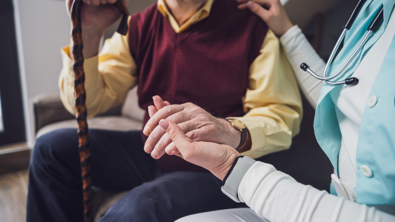 Doctor holding a patient’s hand during a consultation, with another person seated nearby