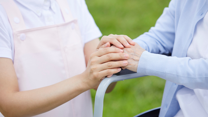 Hands clasped together on a park bench outdoors, with a white and blue shirt visible.