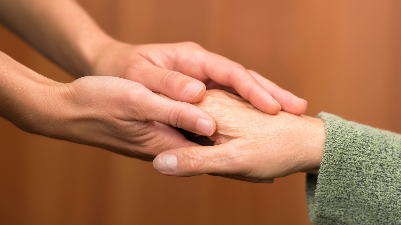 Two hands gently holding a third hand in a supportive gesture on a warm background