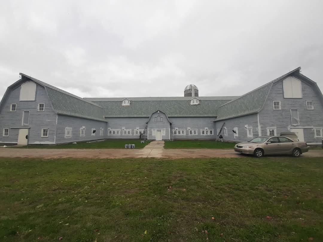 Grey barn with a car parked outside on a cloudy day.