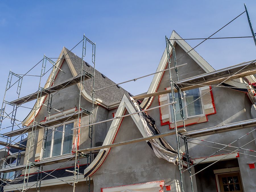 Scaffolding around two gray house roofs under construction against a blue sky