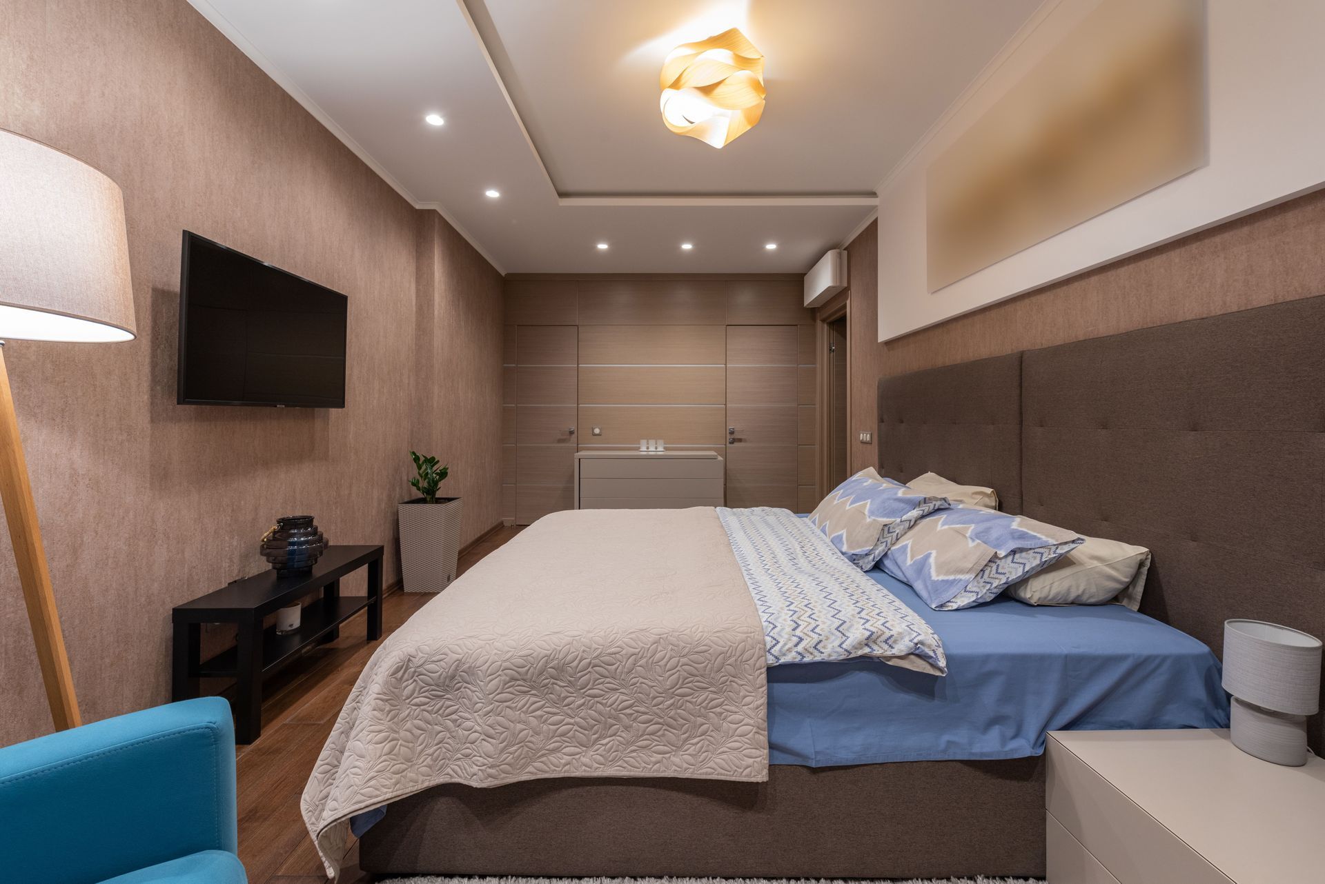 Modern bedroom with a bed, wall-mounted TV, nightstands, and warm recessed lighting
