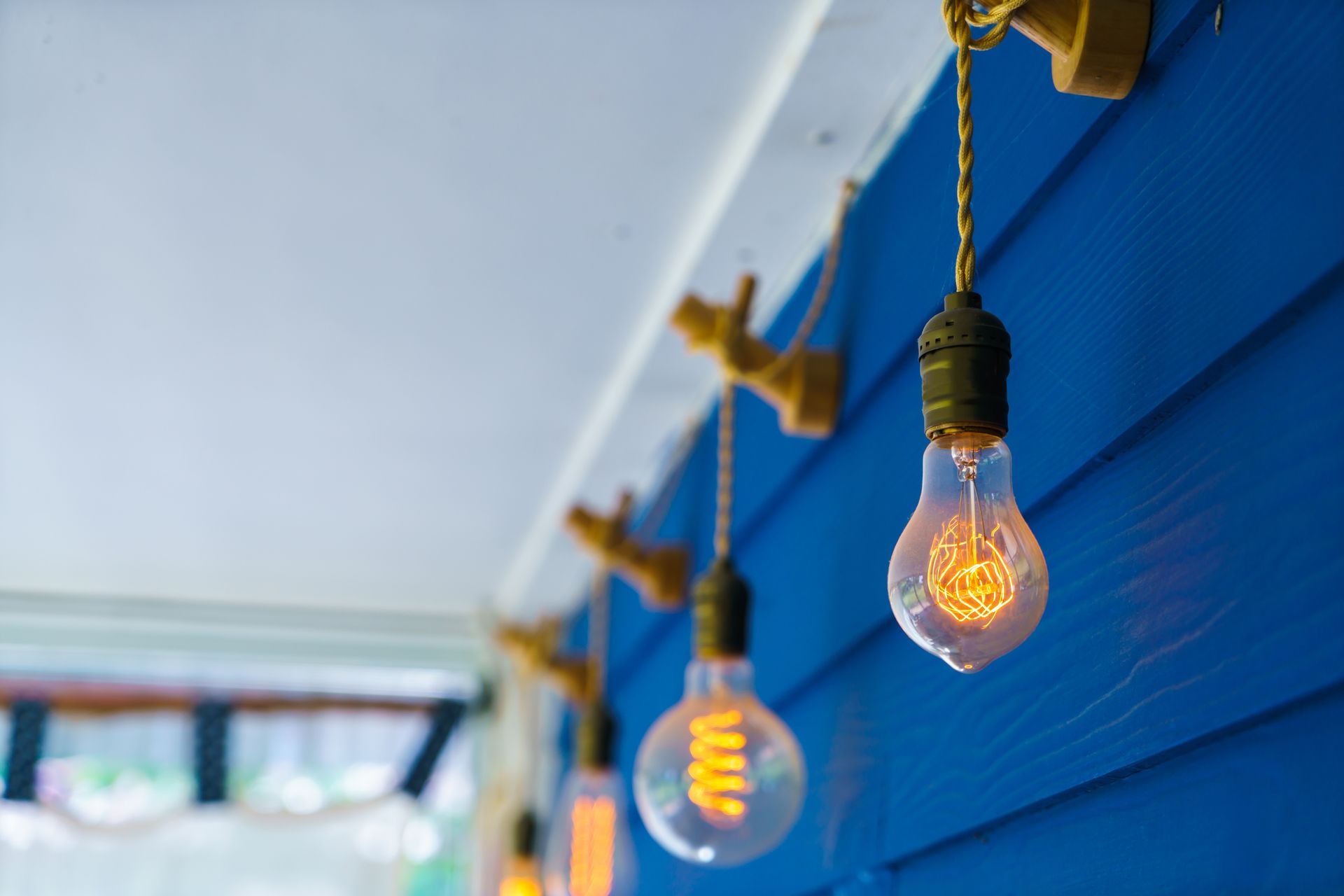 String of lit light bulbs hanging from a blue wall.