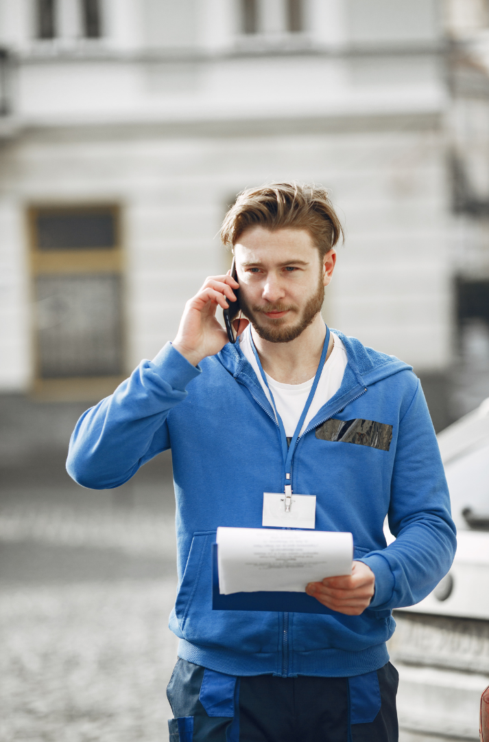 A man is talking on a cell phone while holding a piece of paper.