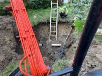 Workers digging near a ladder beside bright orange pipes at a construction site