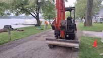 Orange excavator leveling a gravel path beside a lakeside lawn, with orange cones nearby