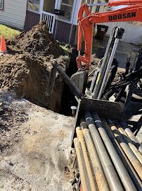 Orange Doosan excavator beside an open trench with piled soil and pipes at a construction site