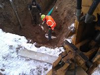Worker in orange safety vest inspecting a snowy excavation site beside heavy machinery