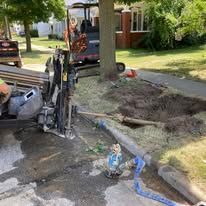 Construction excavator by a torn-up sidewalk and dirt yard in a residential neighborhood