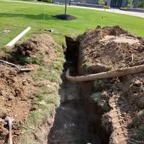 Open trench in a grassy lawn with exposed dirt and a pipe running across it Open trench in a grassy lawn with exposed dirt and a pipe running across it