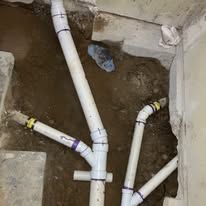PVC drain pipes installed in a dirt trench beside a concrete wall, with yellow tape markings