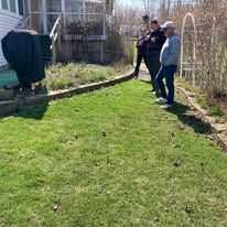 Two people standing on a grassy backyard path beside a fence and garden plants