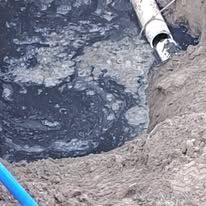 Muddy excavation pit with dark water and a broken white pipe at the edge