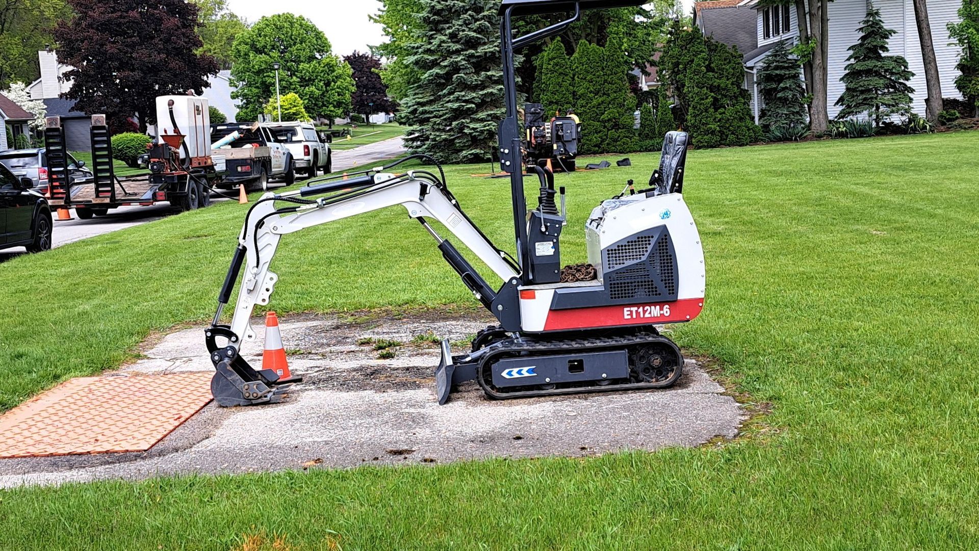 Mini excavator digging gravel on a lawn beside a sidewalk in a suburban yard
