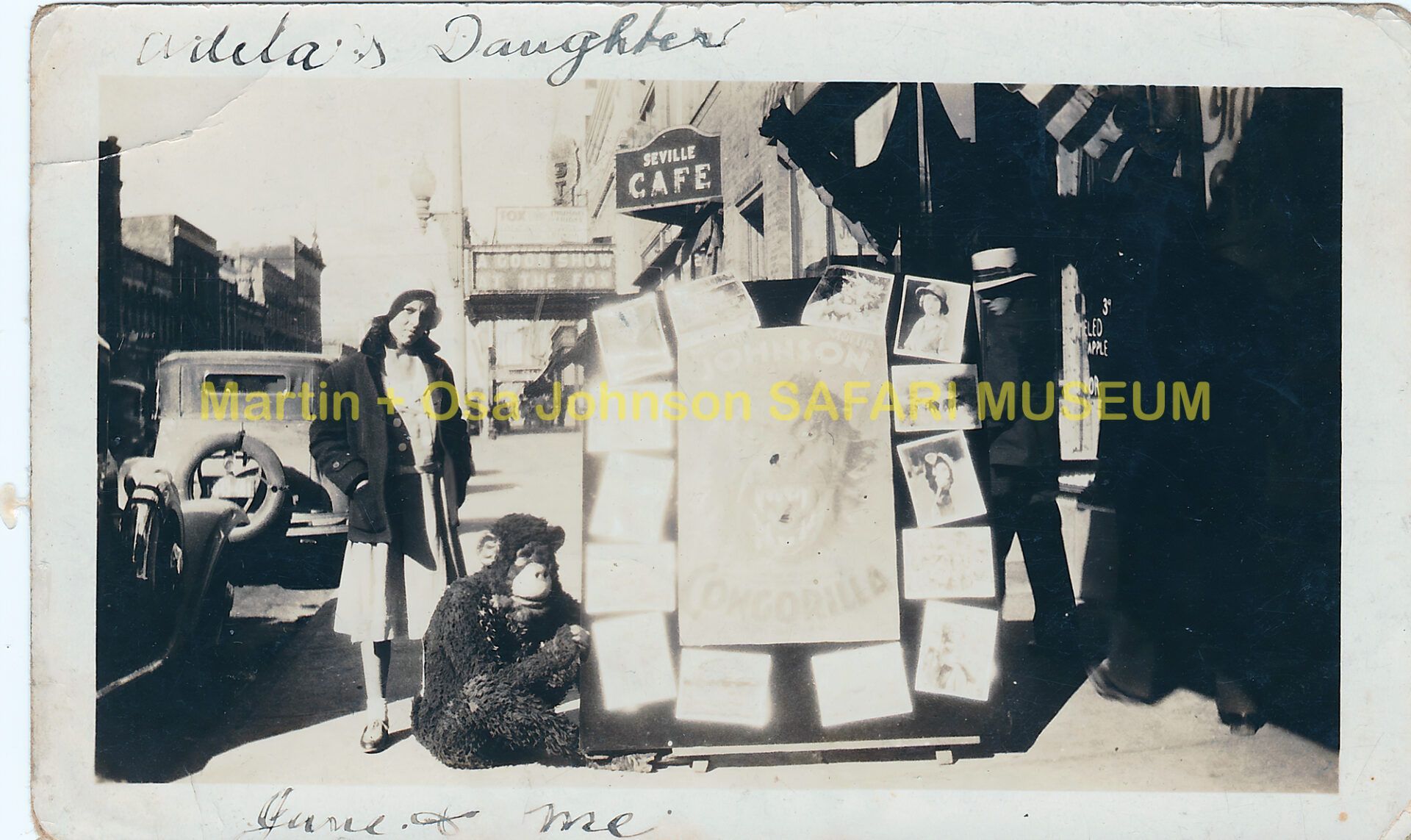 A vintage street scene featuring a person crouching next to a sign displaying portrait photos, with a cafe in the background.