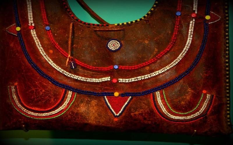 A brown leather bag decorated with curved, multicolored beaded lines, small circular accents, and a central triangle.