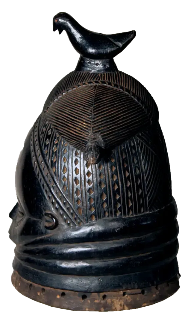 A black, carved wooden Mende Sowei helmet mask with intricate geometric patterns and a bird figure on top.