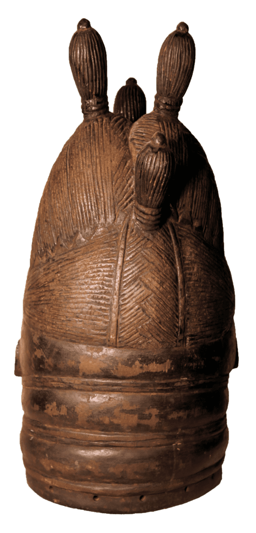 A carved, dark brown wooden helmet mask with a rounded base, textured geometric patterns, and three vertical protrusions.