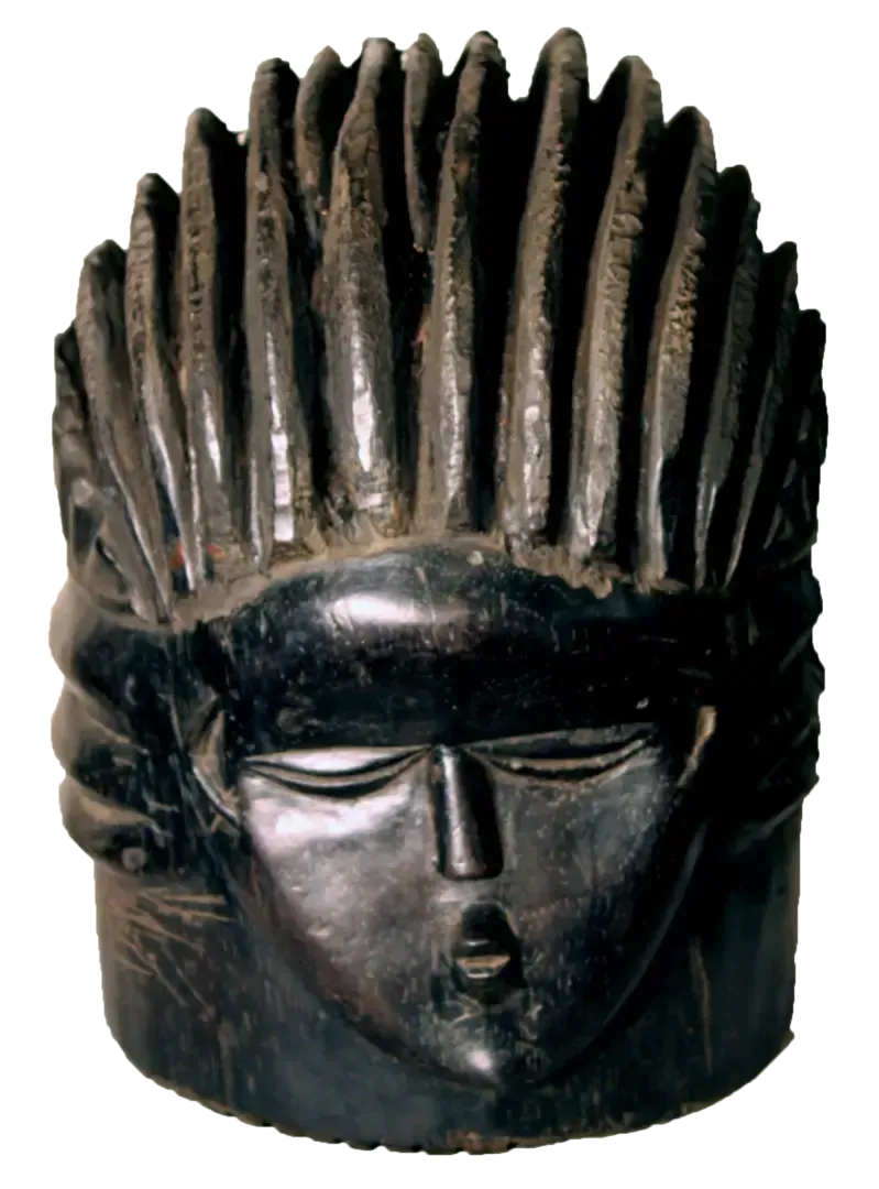 Dark, carved wooden sculpture of a stylized face with a prominent, ridged, fan-like hairstyle.